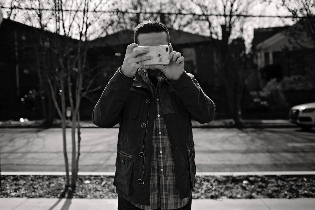 Black and white shot of faceless man in casual clothes standing on pavement and taking photo on smartphone